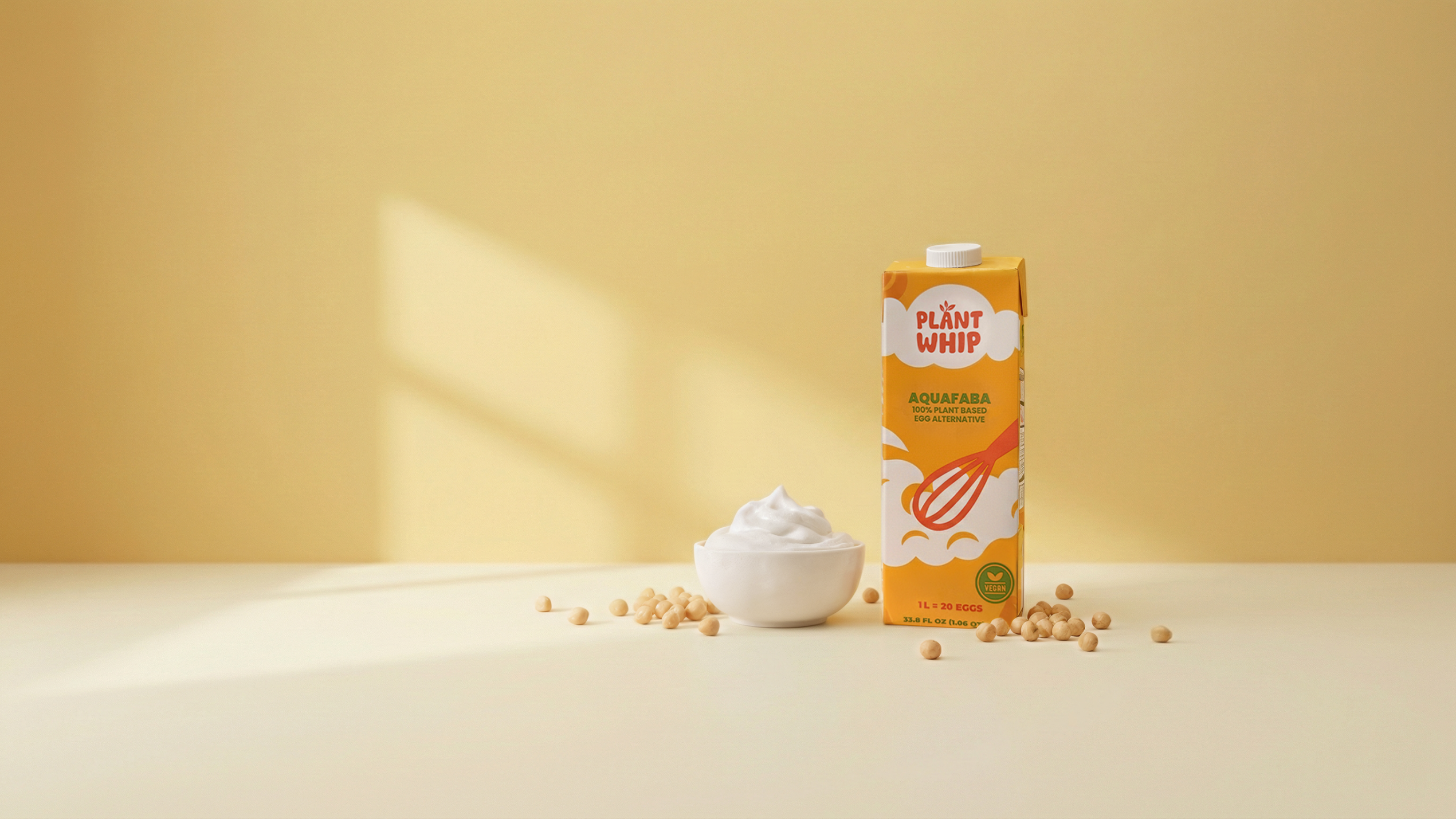 Carton of PlantWhip brand product with a bowl of whipped cream and scattered chickpeas on a beige background